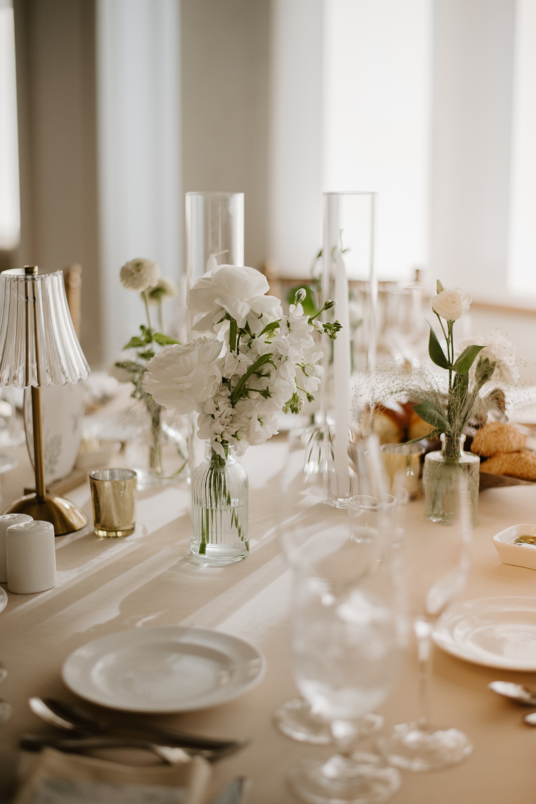 Close-up of an elegant wedding table setting with white flowers in a glass vase and soft golden light.